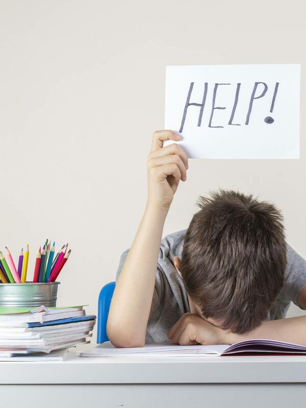 ein Junge sitzt an einem Schreibtisch, legt seinen Kopf darauf und hält ein Schild mit "Hilfe"